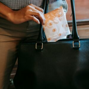 Crop faceless female in casual clothes putting panty liner in package in black leather handbag